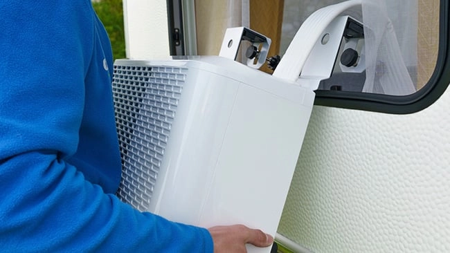 Schritt 3: Wie montiert man eine Split-Klimaanlage Weiße tragbare Kühlbox wird von einer Person in blauer Kleidung in einem Wohnwagen oder Wohnmobil installiert