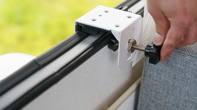Schritt 3a wie montiert man eine Split-Klimaanlage Weißer Befestigungsclip für Markise wird mit einem Drehknopf an einer Schiene festgezogen, vor einem hellgrünen Hintergrund