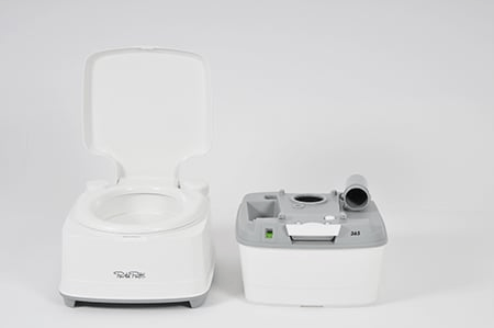 Zwei Teile einer Porta Potti Campingtoilette Tragbare Toilette mit offenem Deckel neben einem abnehmbaren Abfalltank-Teil auf grauem Hintergrund