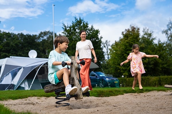 Kinder spielen auf einer Wippe bei einem Campingplatz mit Zelt im Hintergrund unter blauem Sommerhimmel. Kinder, die auf dem Spielplatz auf dem Campingplatz spielen, mit einem Zelt im Hintergrund.