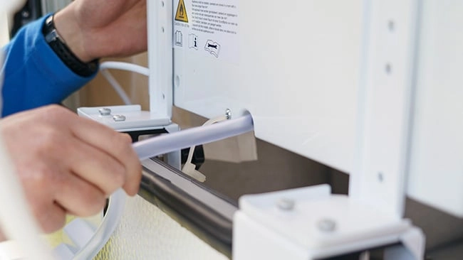 Schritt 5: Wie montiert man eine Split-Klimaanlage Ein Techniker installiert oder repariert ein weißes Gerät mit Warnhinweisen und verwendet dabei ein graues Werkzeug, um ein Teil zu befestigen.