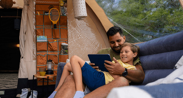 Vater und Sohn auf aufblasbarem Sofa Gemütliches Zeltinneres mit aufblasbaren Möbeln und organisierter Campingausrüstung an der Zeltwand im Hintergrund