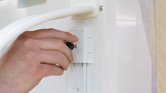 Schritt 4c wie installiert man eine Split-Klimaanlage Hand, die ein weißes Scharnier oder einen Befestigungsmechanismus an einer Tür oder einem Fensterrahmen mit einem Schraubenzieher festschraubt